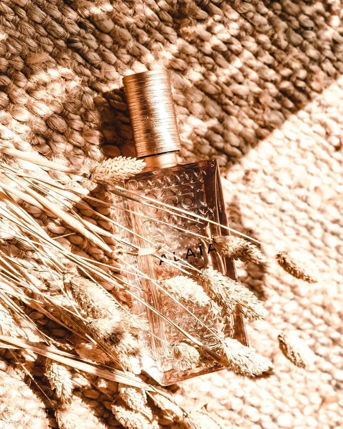 Rose-gold bottle among dried wheat on woven jute
