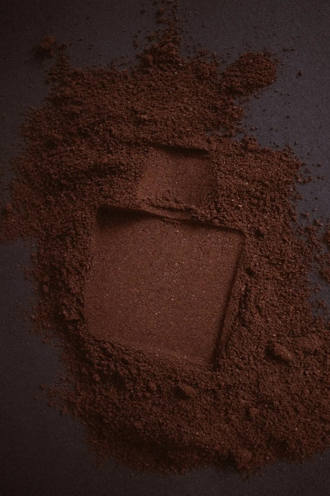 Bottle pressed into a bed of cocoa powder, leaving its shape behind