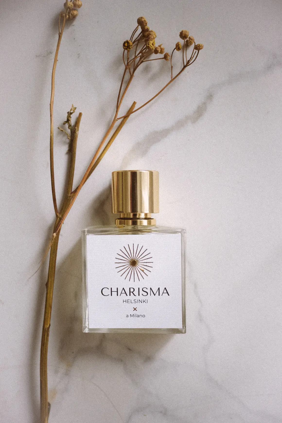 Charisma Helsinki bottle on pale marble beside a dried flowering stem