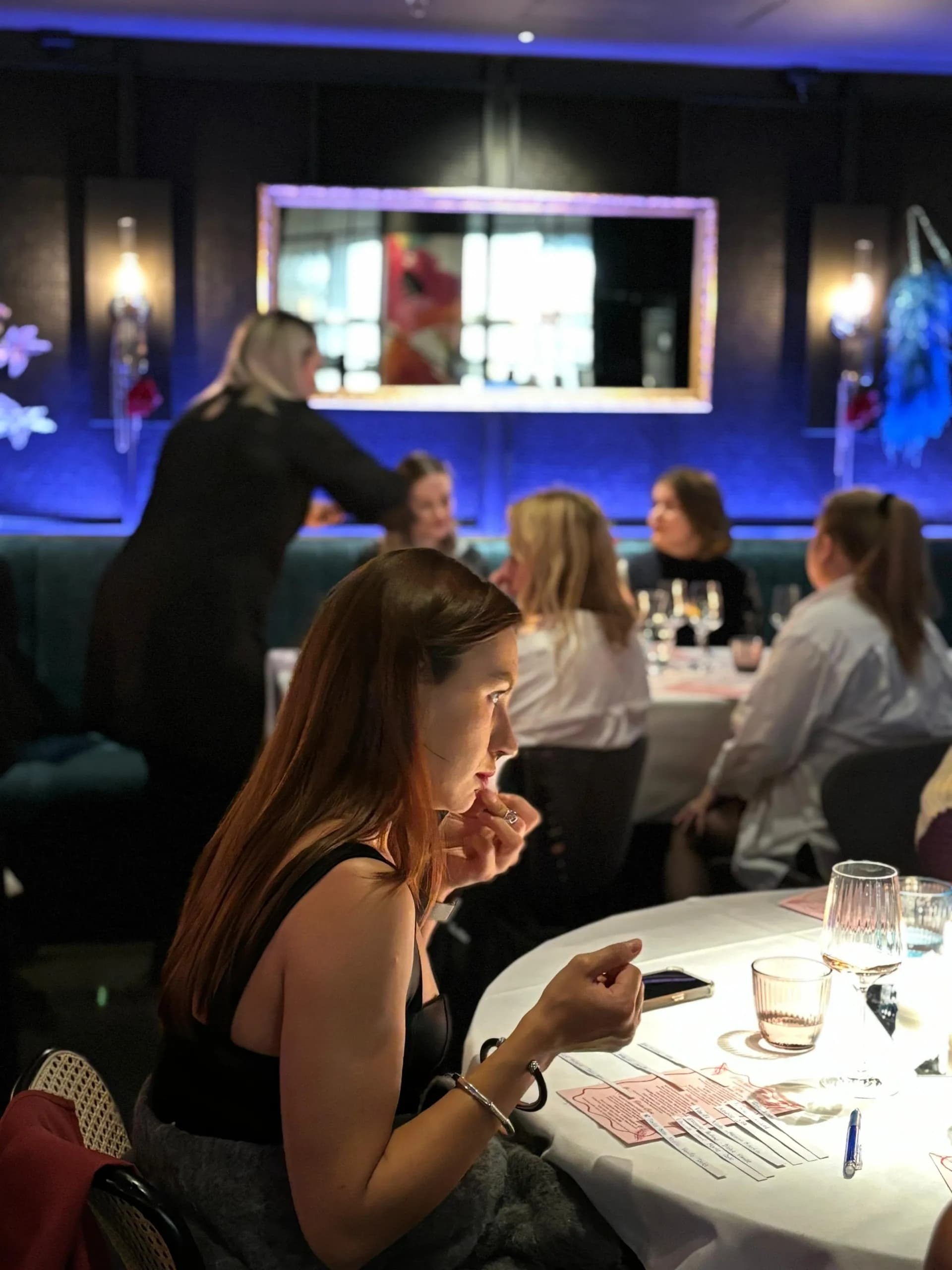 A guest smelling from the back of the hand at a Scent Match evening, tables of guests behind